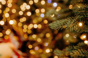 A close-up of a Christmas tree branch with warm fairy lights, with golden festive lights softly blurred in the background.